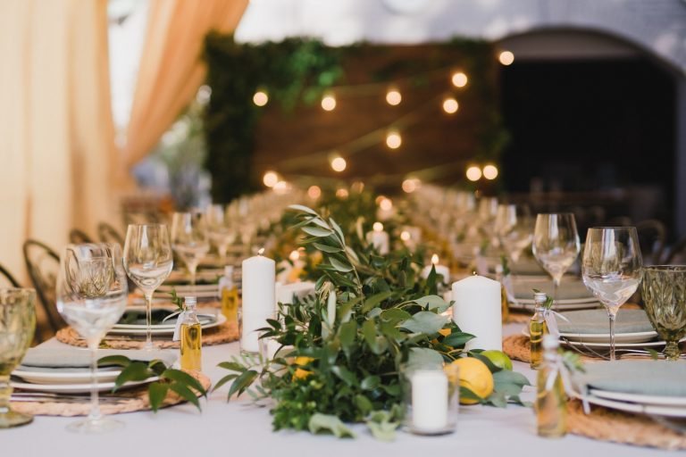 Coziness and style. Modern event design. Table setting at wedding reception. Floral compositions with beautiful flowers and greenery, candles, laying and plates on decorated table.