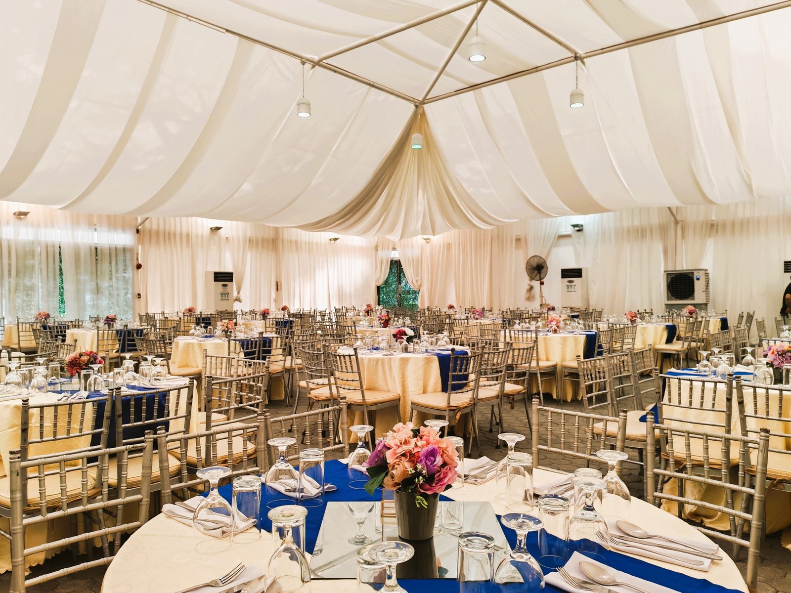 : Elegant tent wedding reception at Light of Love Trust venue with draped ceiling and blue table linens.