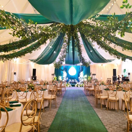 A stunning wedding reception layout in a Quezon City hall featuring lush green and white ceiling drapes and a central aisle runner.
