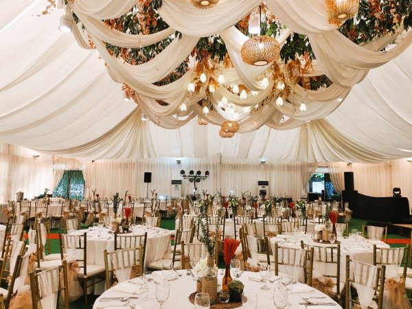 A grand wedding reception venue in Quezon City featuring cream ceiling drapes, warm pendant lights, and gold Tiffany chairs for a large guest count.