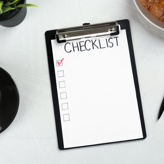 A top-down view of a checklist on a black clipboard next to a cup of coffee and a croissant, illustrating the final review and administrative oversight phase of a corporate event checklist.