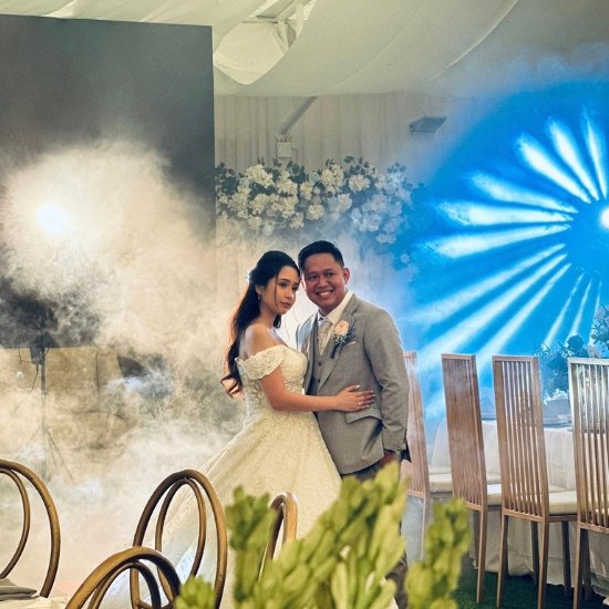A bride and groom posing amidst dramatic stage fog and blue starburst lighting at a wedding venue in Quezon City.